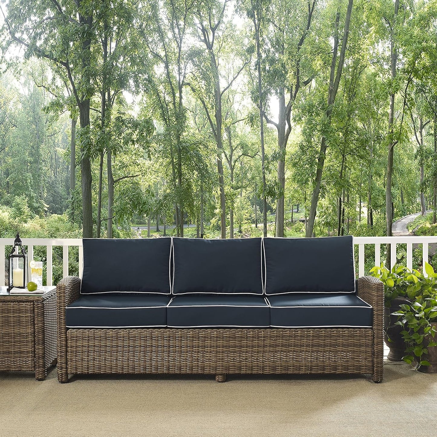 Brown Wicker Outdoor Sofa with Navy Cushions sits on a porch surrounded by trees, showcasing its comfort and style.