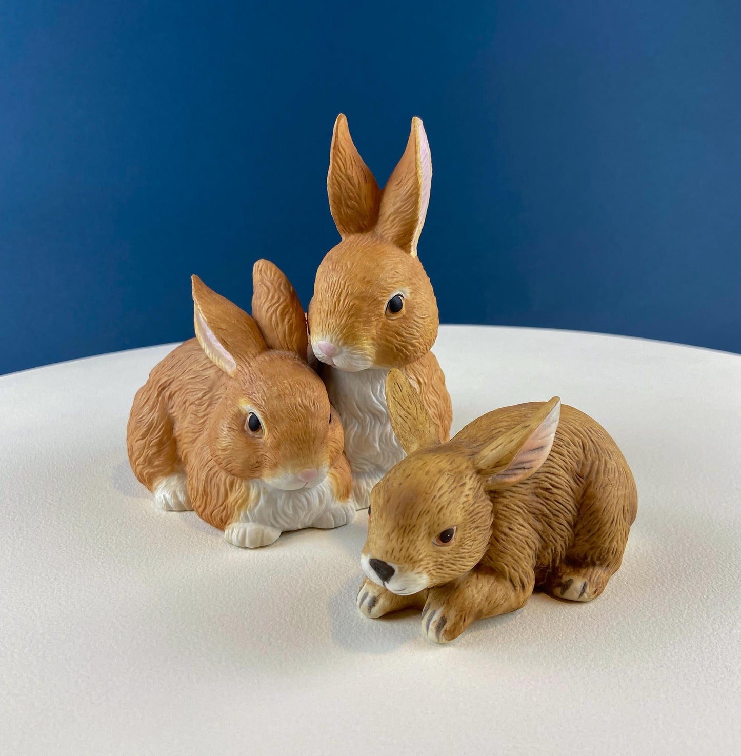 Three rabbit figurines on a white surface with a blue background