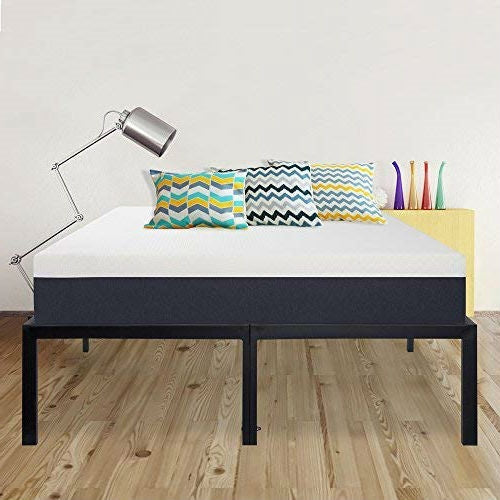 Bed with black frame, white mattress, colorful pillows, and a lamp on a wooden floor.