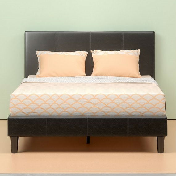 Bed with black headboard, beige bedding, and pillows against a light green wall.