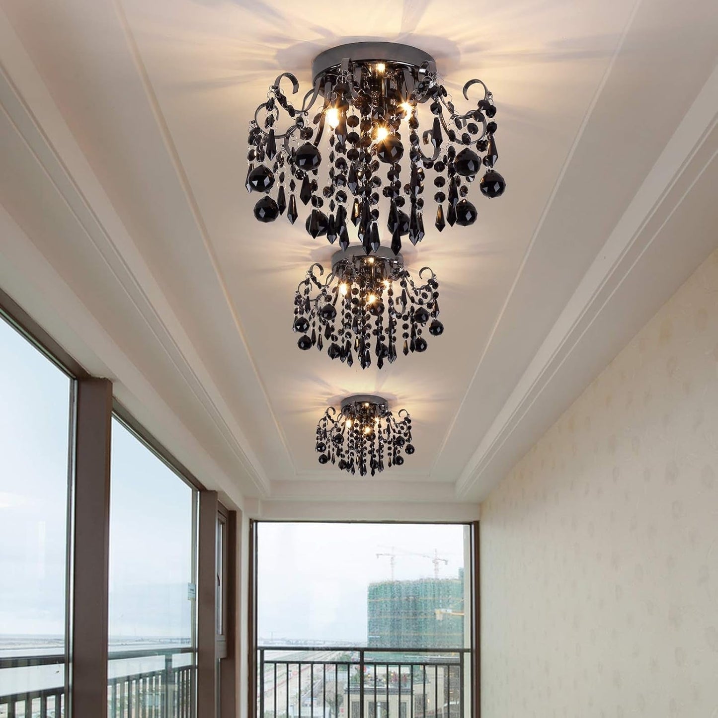 Chandelier hanging from a ceiling with a view of a balcony and cityscape outside.