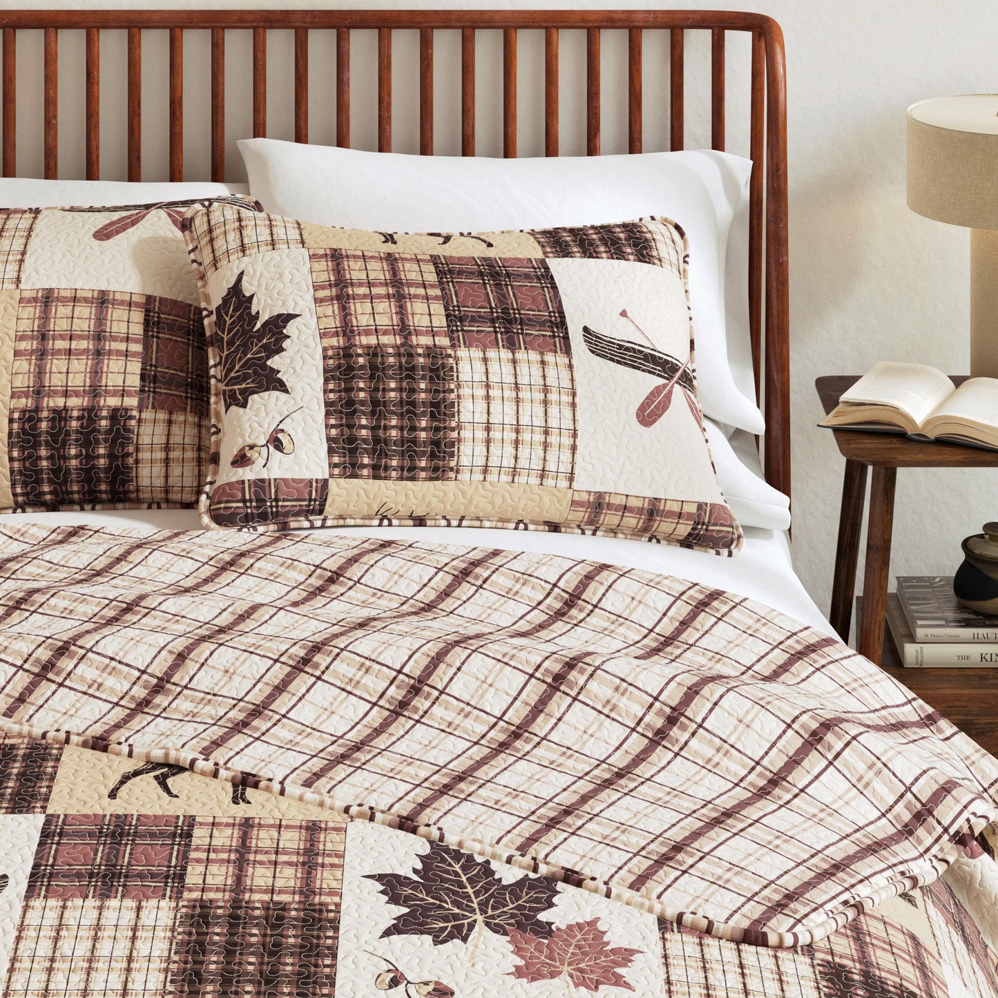 Bed with plaid and leaf patterned bedding, wooden headboard, and lamp.