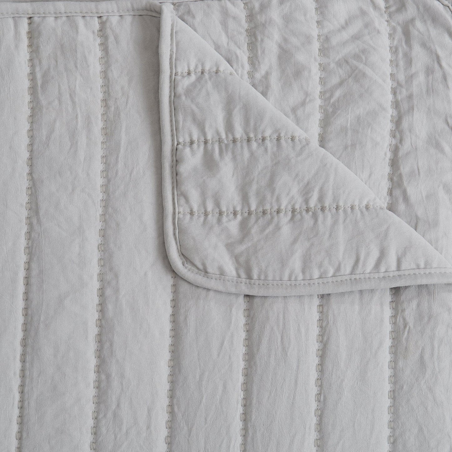 Gray quilt with a textured pattern and visible stitching on a matching background