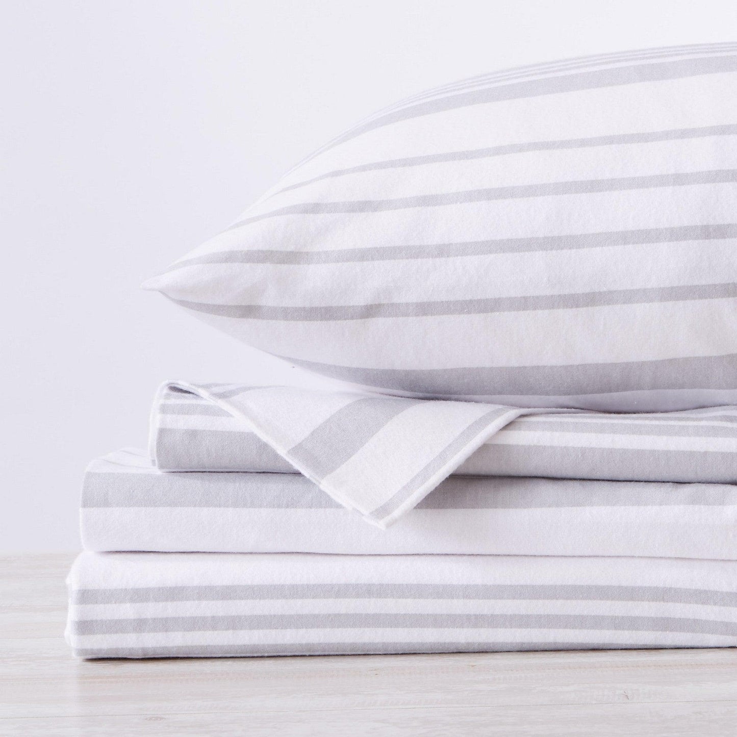 Stack of white striped bed sheets and pillowcases on a light gray background