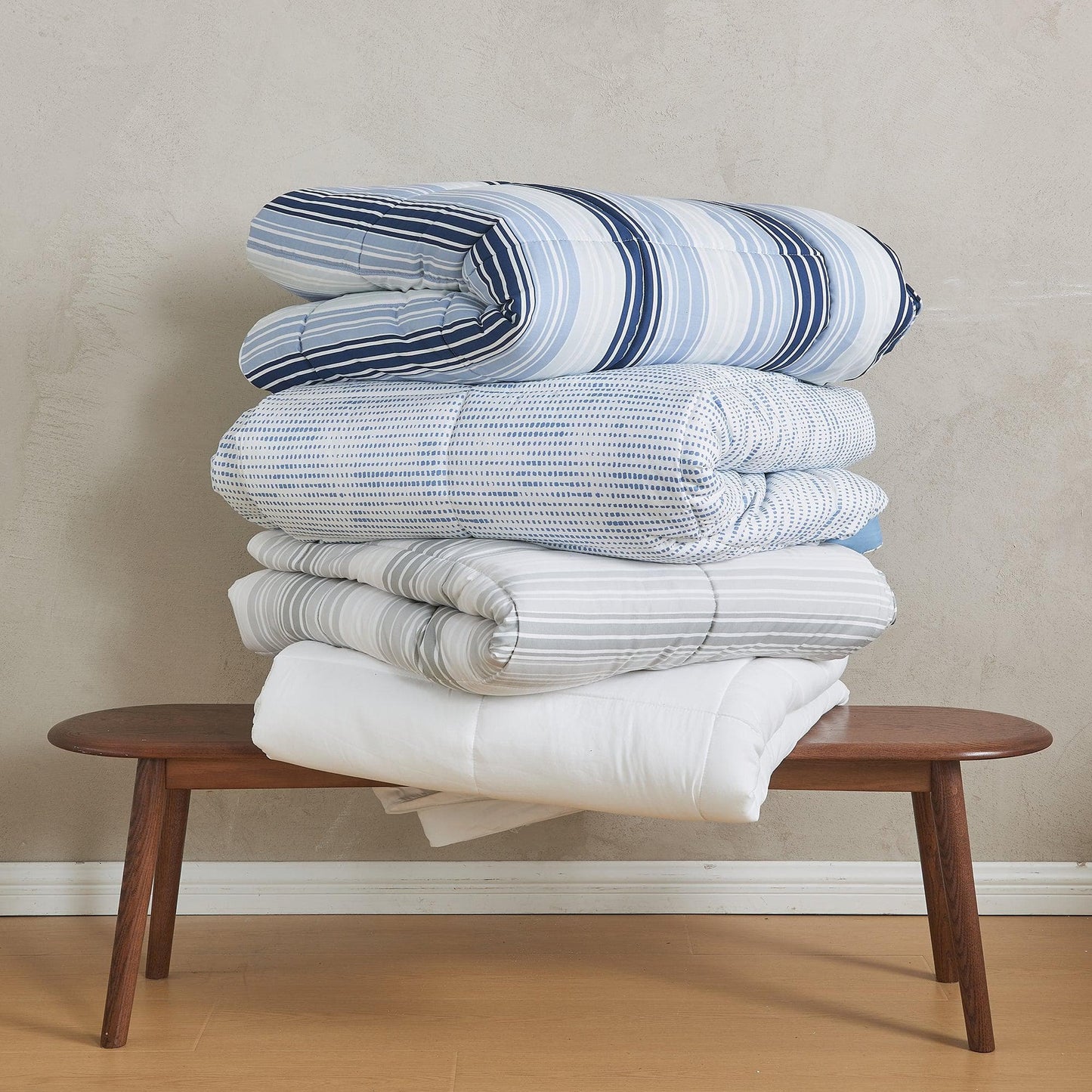 Stack of striped blankets on a wooden bench against a beige wall.