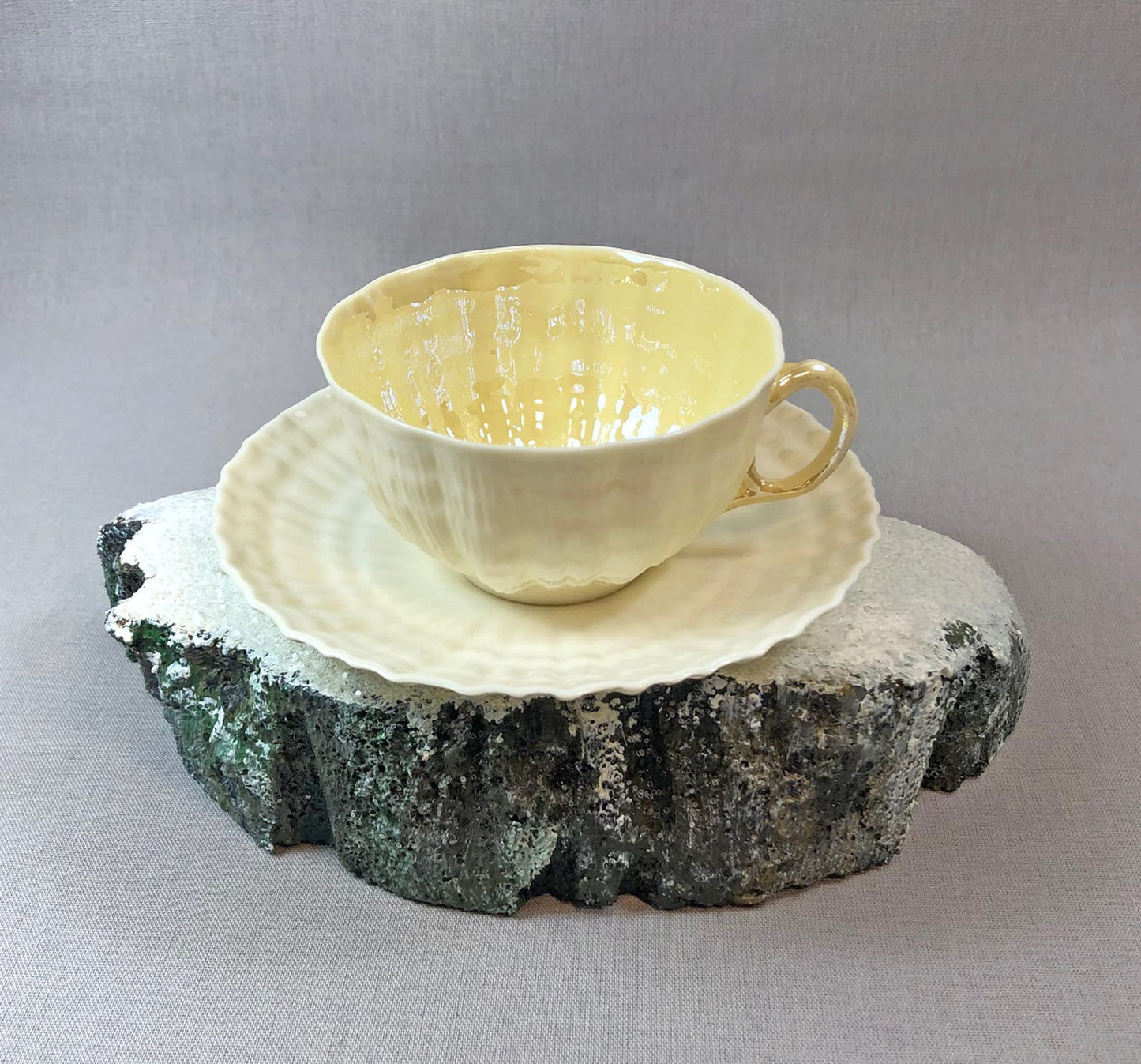 Yellow ceramic teacup and saucer on a textured stone surface with a gray background