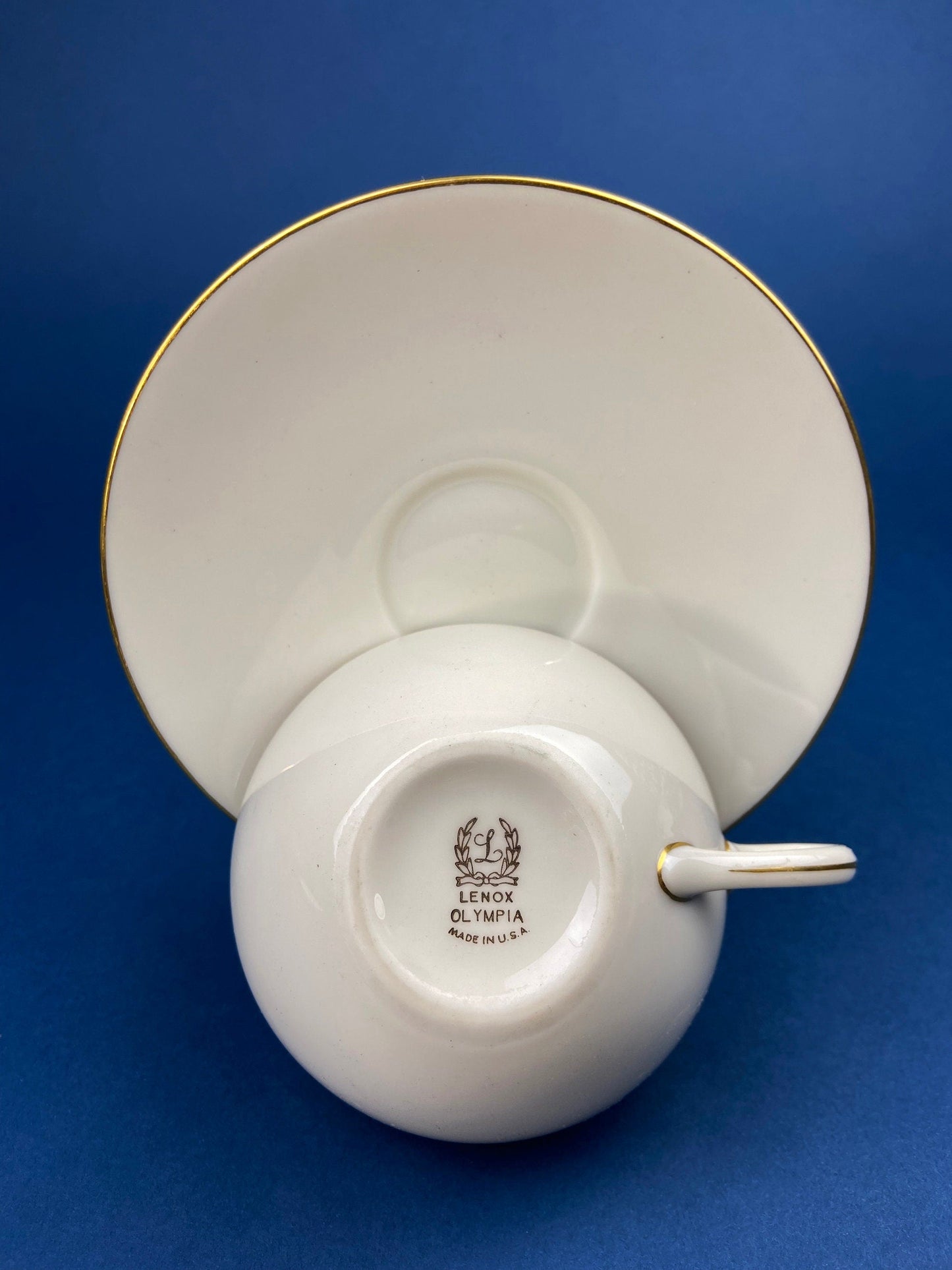 White teacup and saucer with gold trim on a blue background
