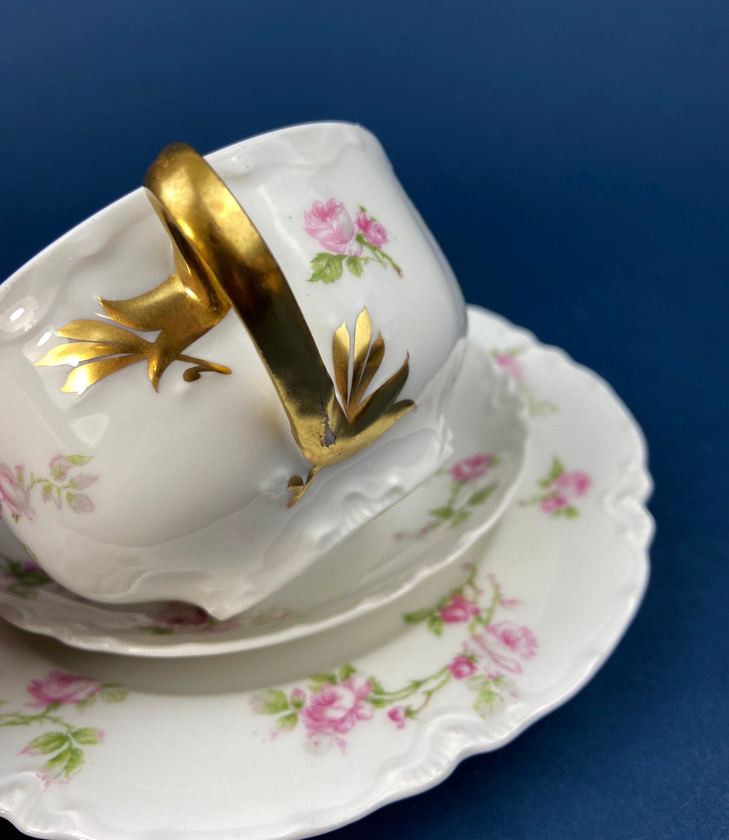 White teacup with gold accents and floral patterns on a matching saucer against a blue background