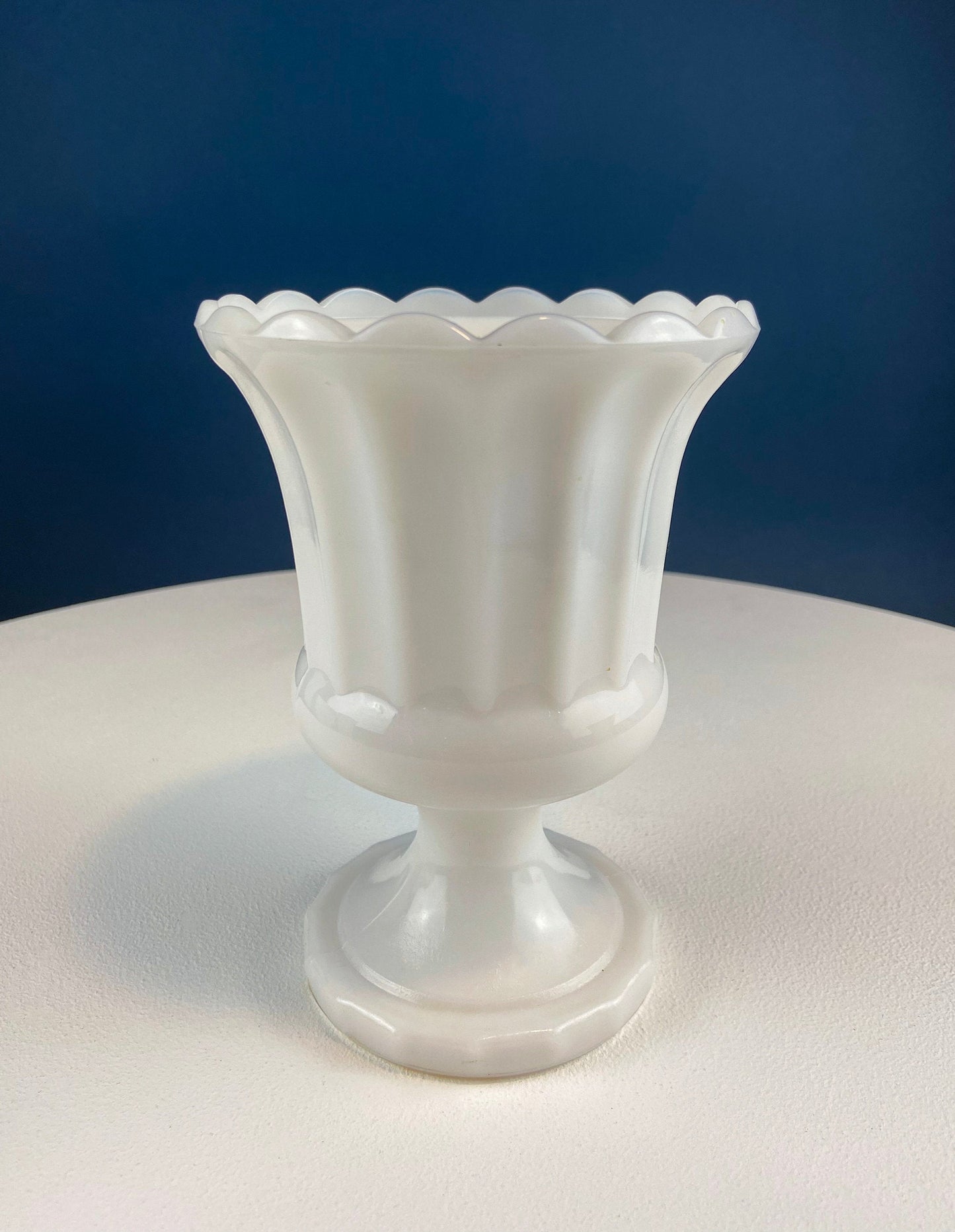 White ceramic vase with scalloped rim on a white surface with a blue background
