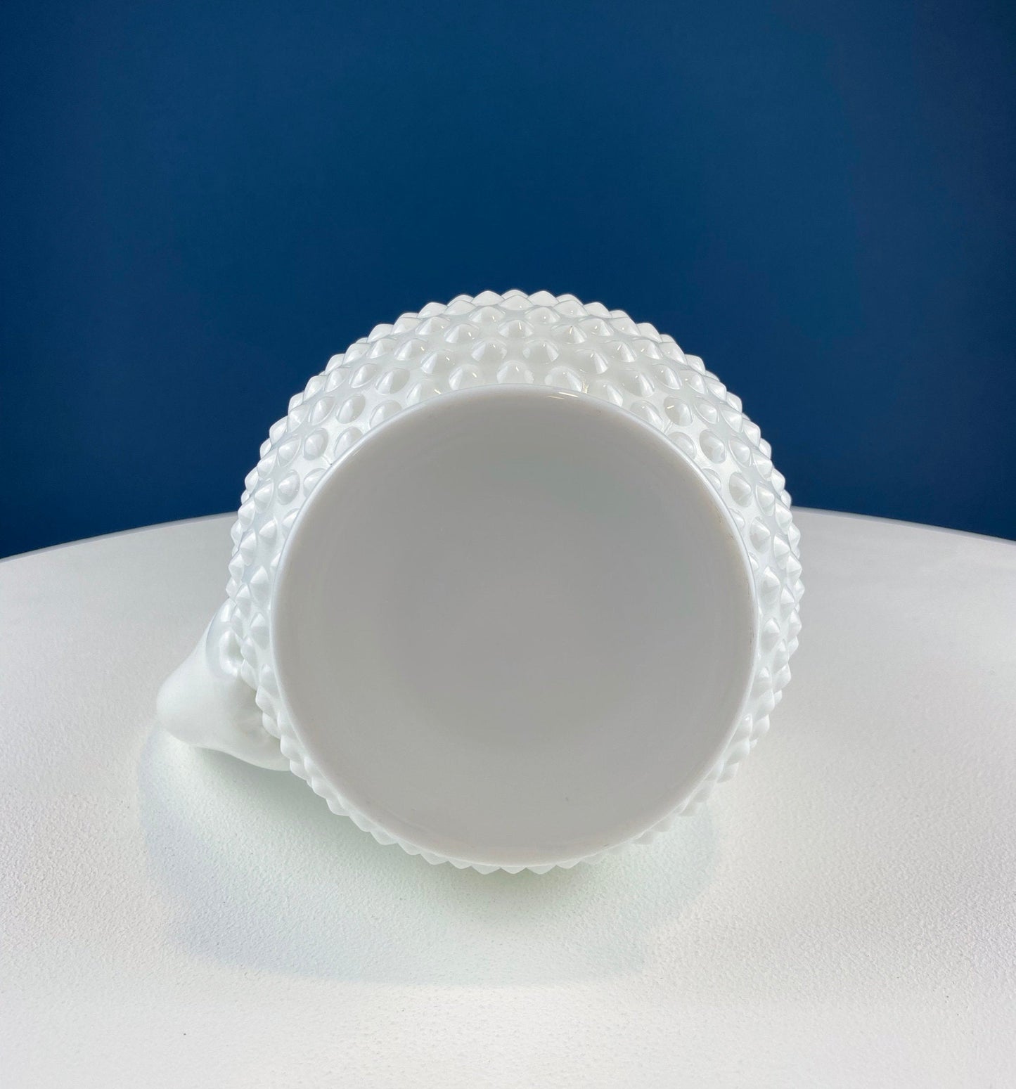 White ceramic cup with textured rim on a white surface against a blue background
