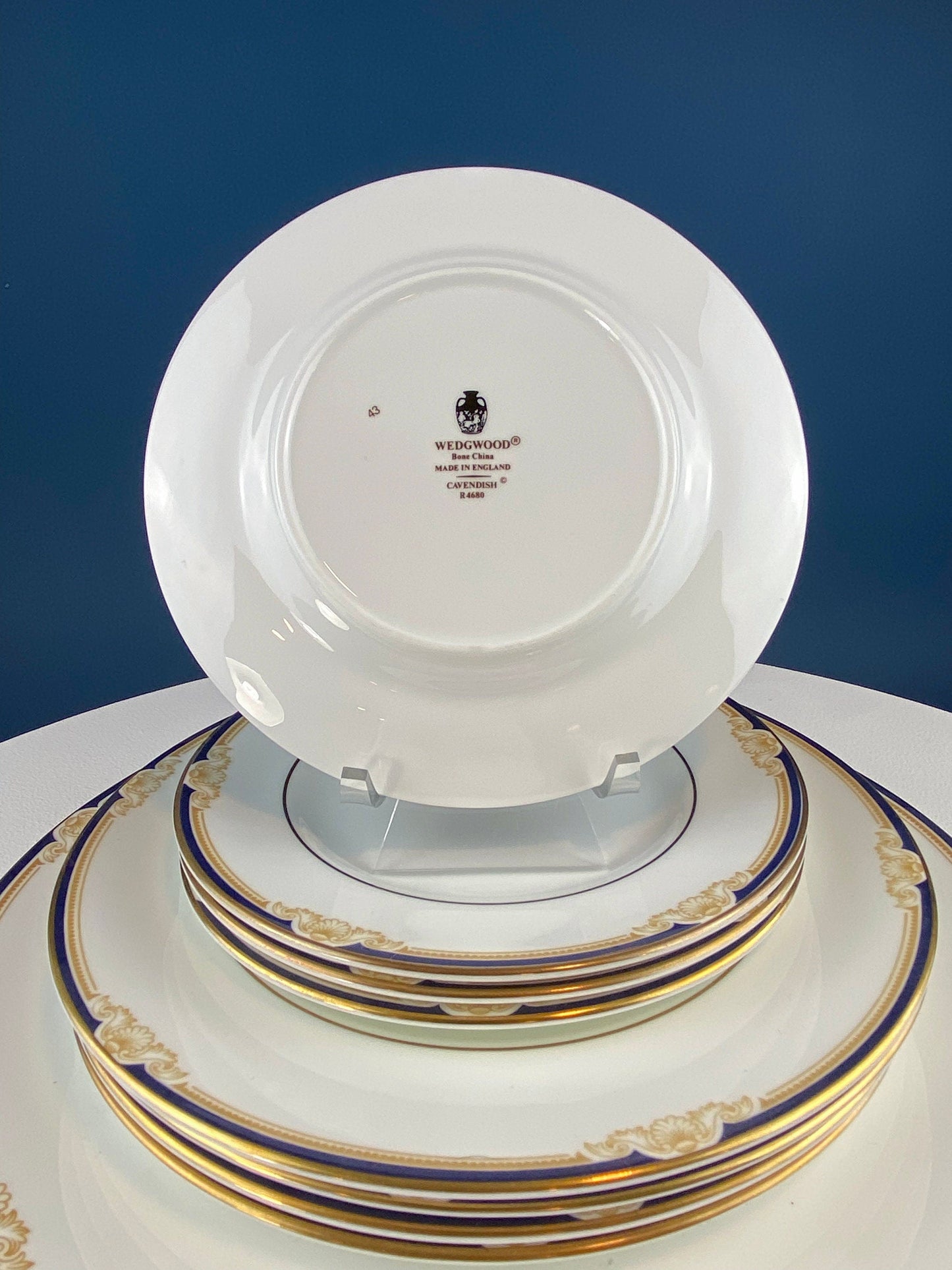 Set of white plates with gold and blue rims on a white surface against a blue background