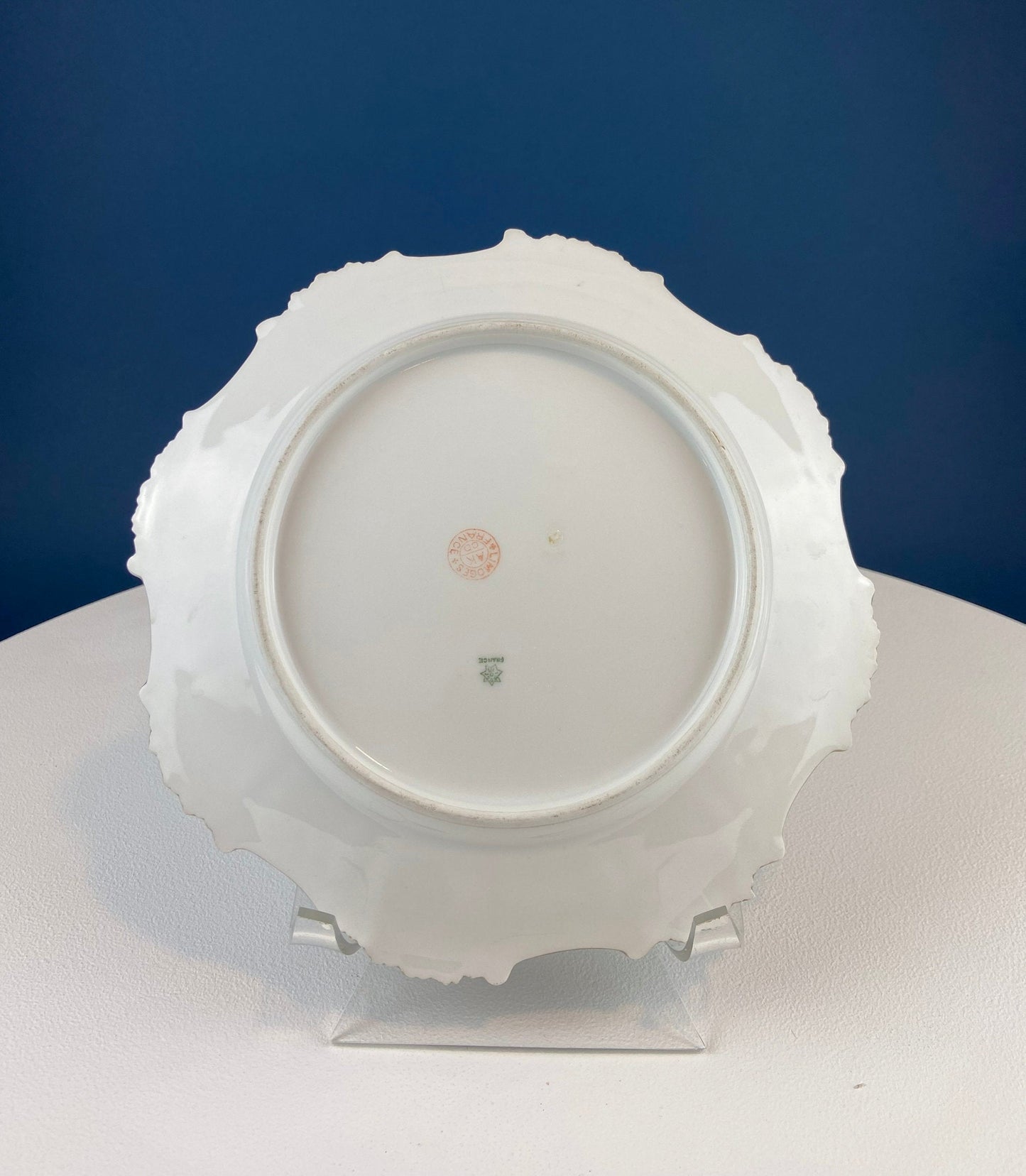 White ceramic plate with decorative rim on a stand against a blue background