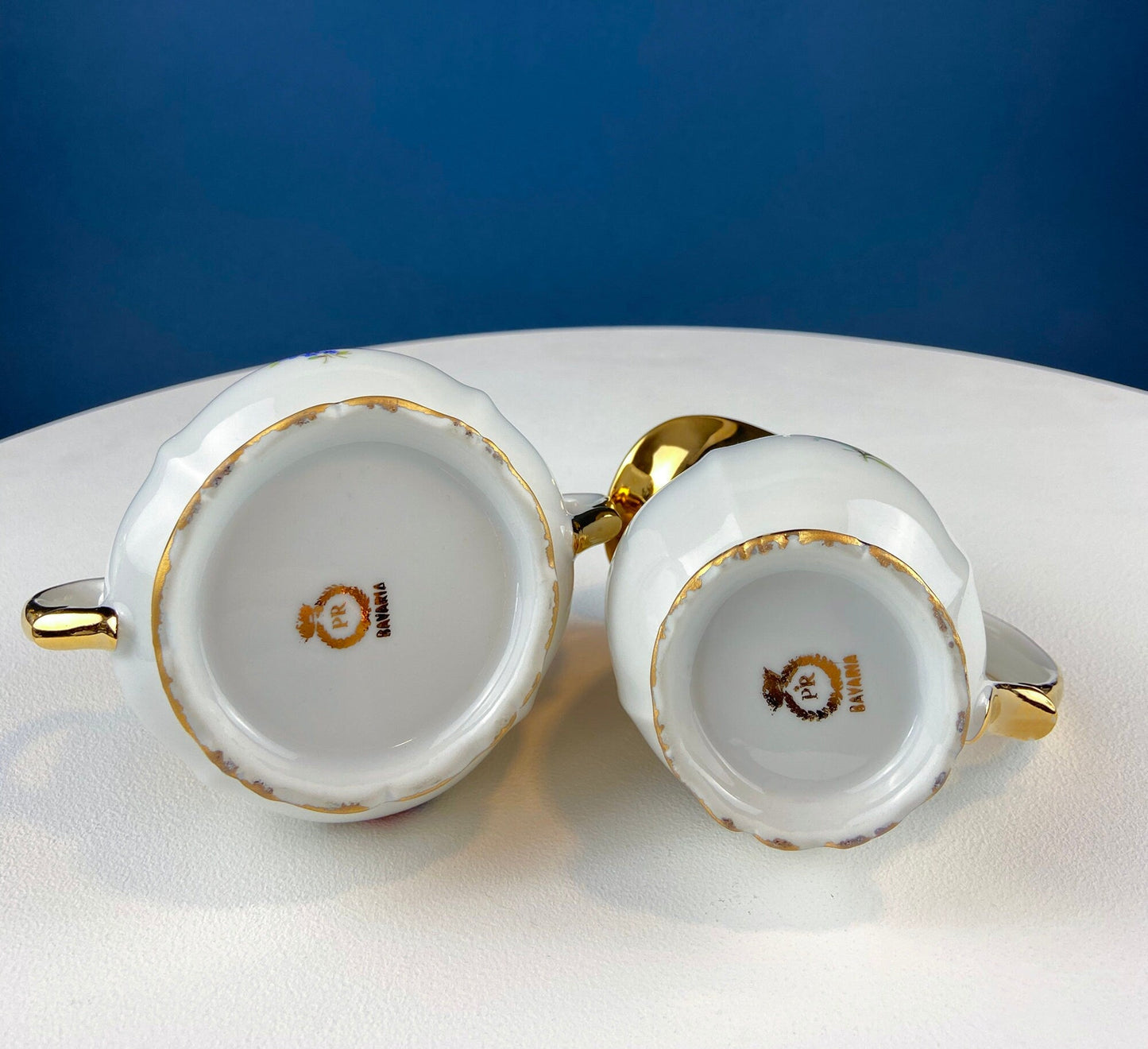 Two white ceramic teapots with gold accents on a white surface with a blue background