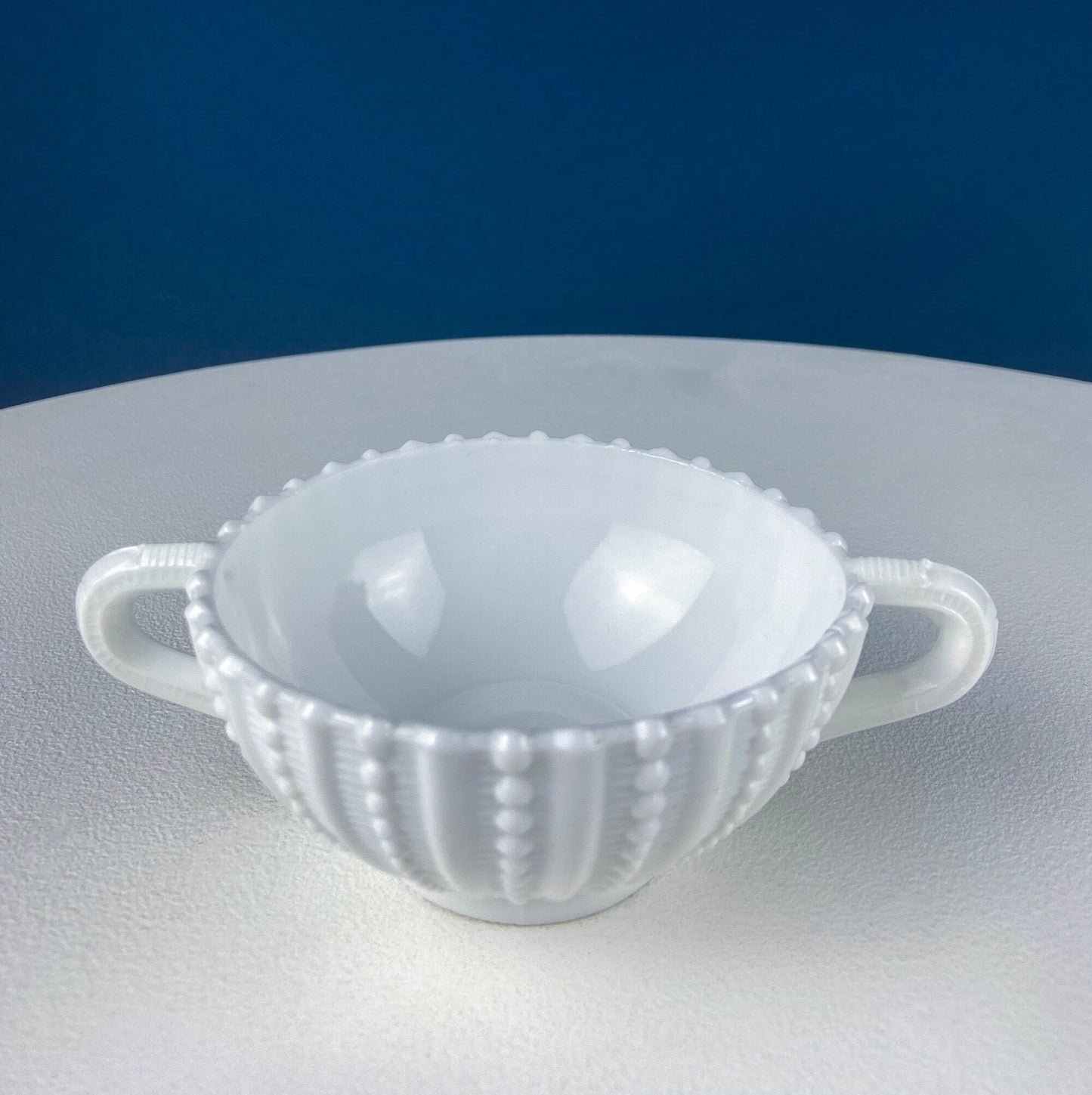 White milk glass sugar bowl with handles on a white surface with a blue background