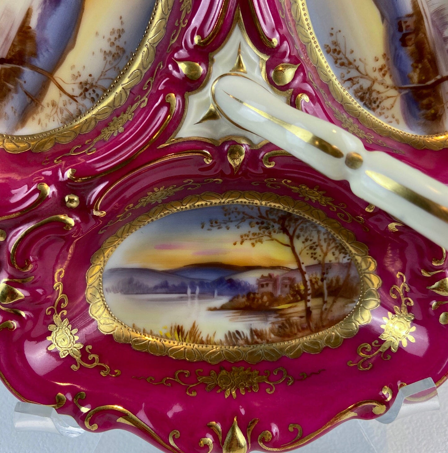 Decorative plate with pink border, gold detailing, and scenic painting on a white background
