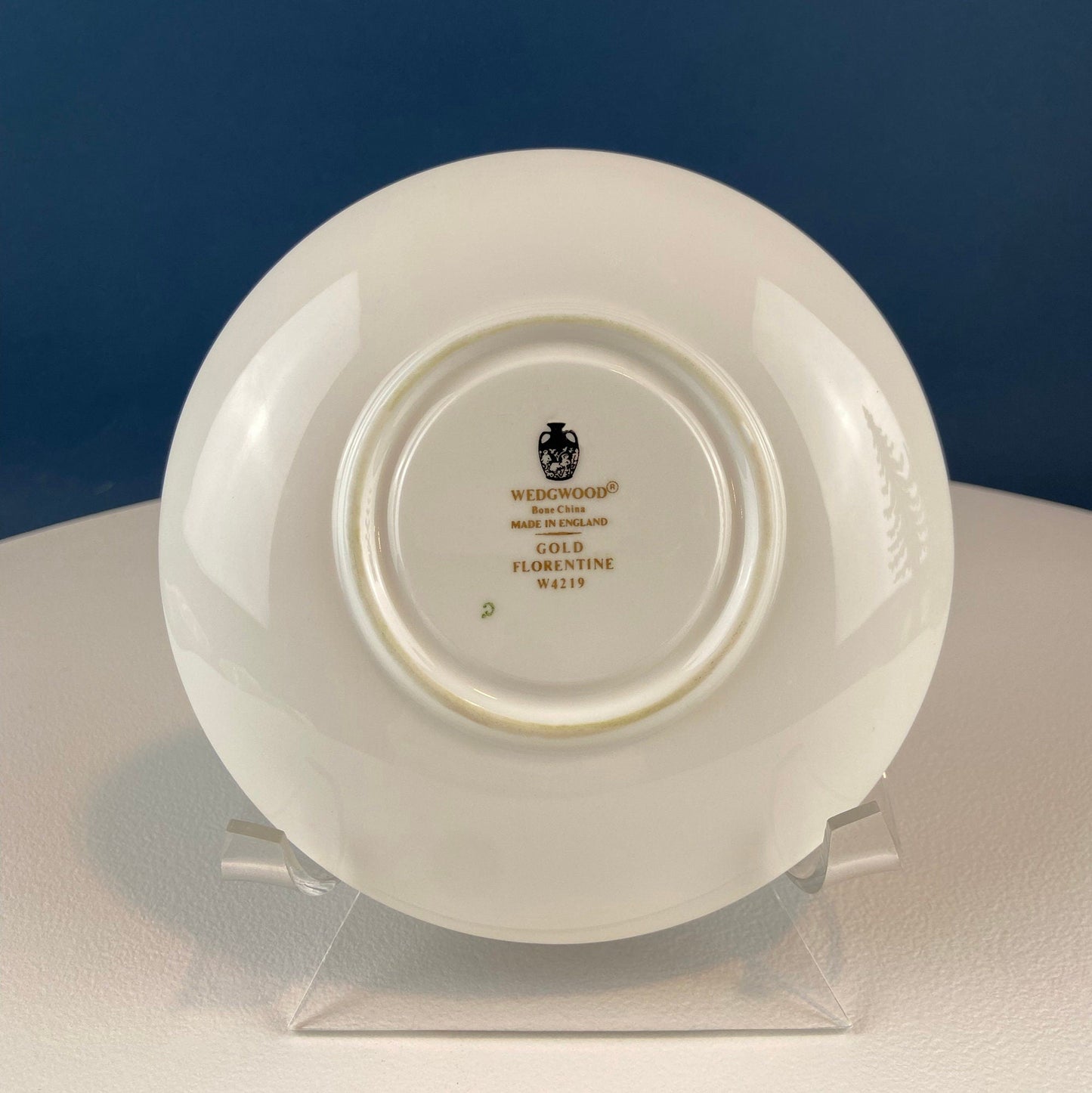 White ceramic plate with 'WEDGWOOD' branding on a clear stand against a blue background