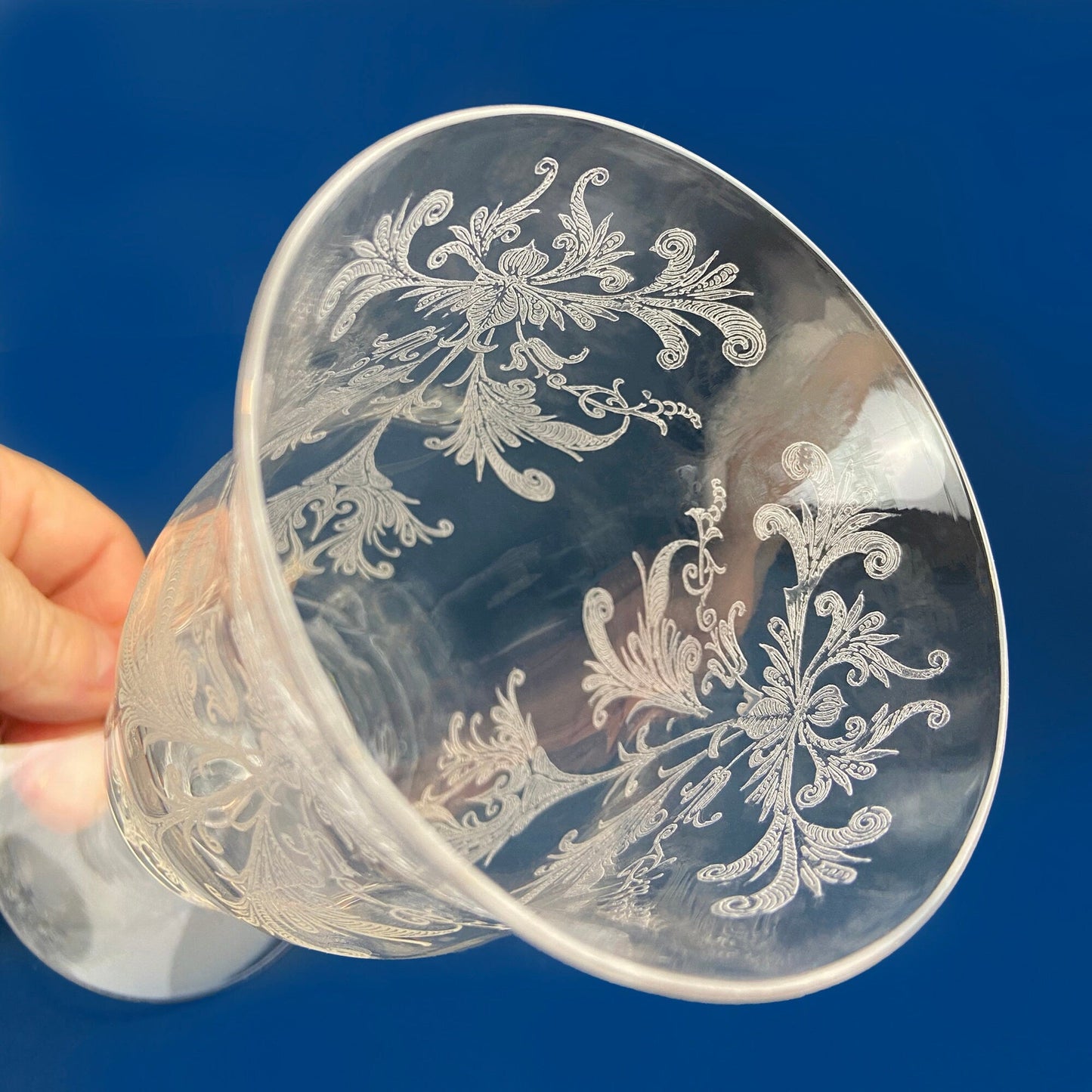 Clear glass goblet with intricate white floral patterns against a blue background