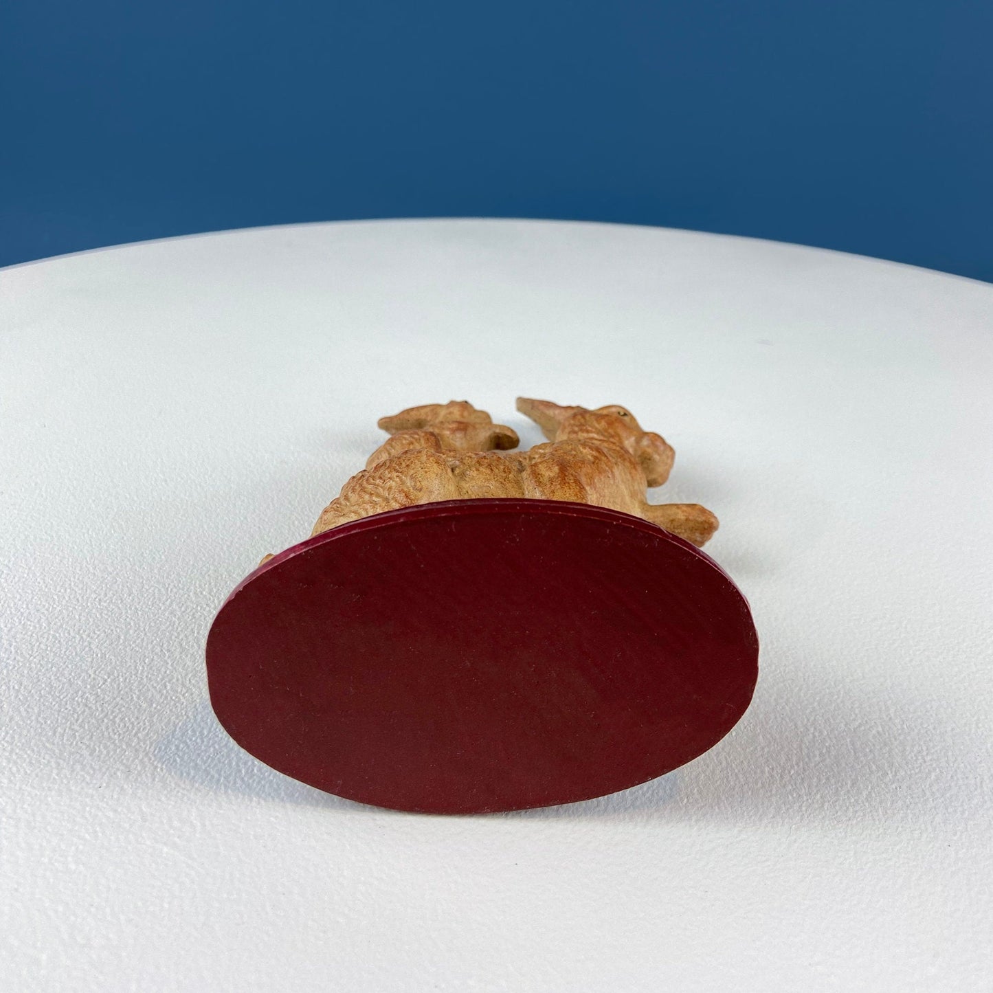 Decorative rabbit figurine with a red oval base and brown top on a white surface with blue background