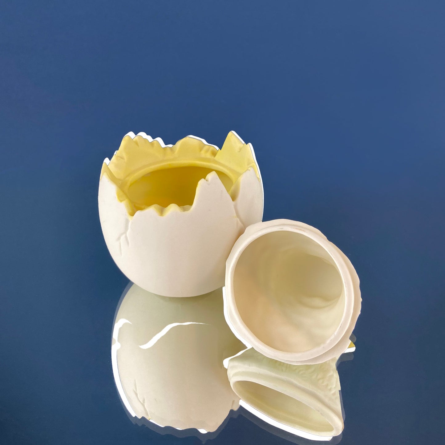 Broken eggshell with yellow yolk on a reflective blue surface