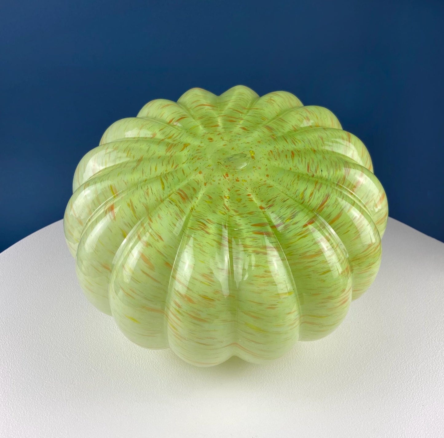 Green glass sculpture on a white platform with a blue background