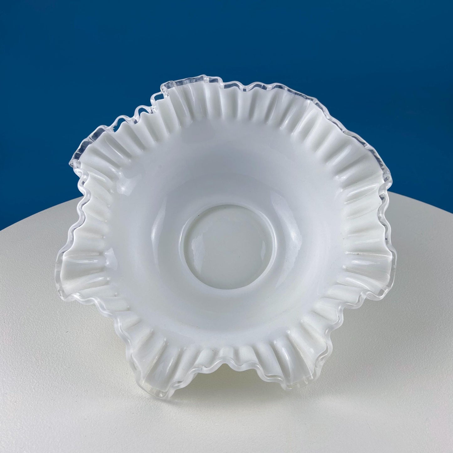 White glass bowl with decorative edge on a white surface with blue background