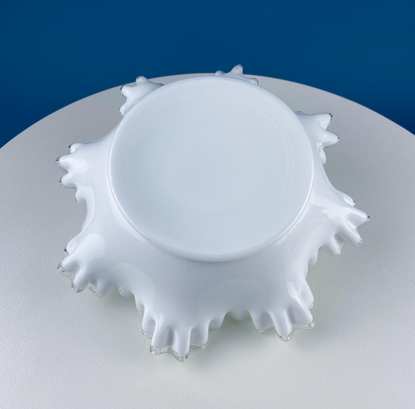 White glass bowl on a white surface with a blue background