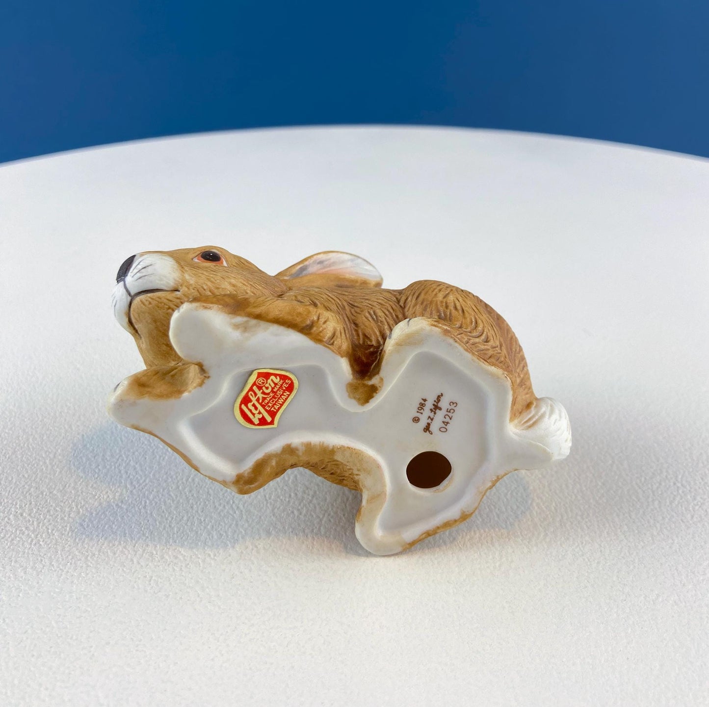 Ceramic rabbit-shaped figurine on a white surface with a blue background