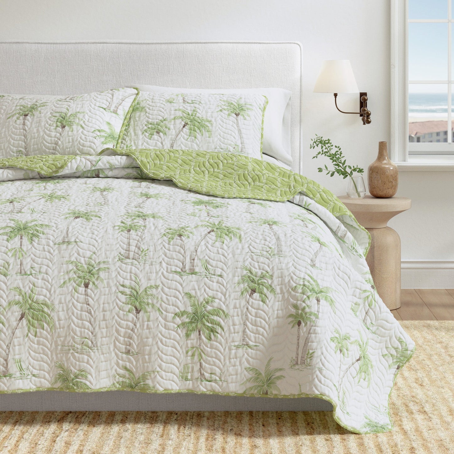 Bed with green and white patterned quilt and pillows in a bright bedroom.