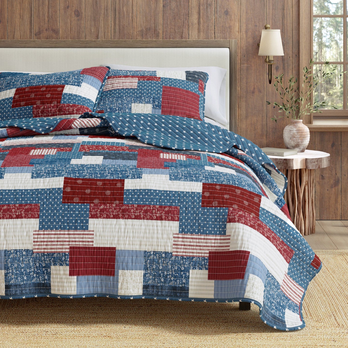 Quilt with red, white, and blue pattern on a bed in a room with wooden walls and a lamp.