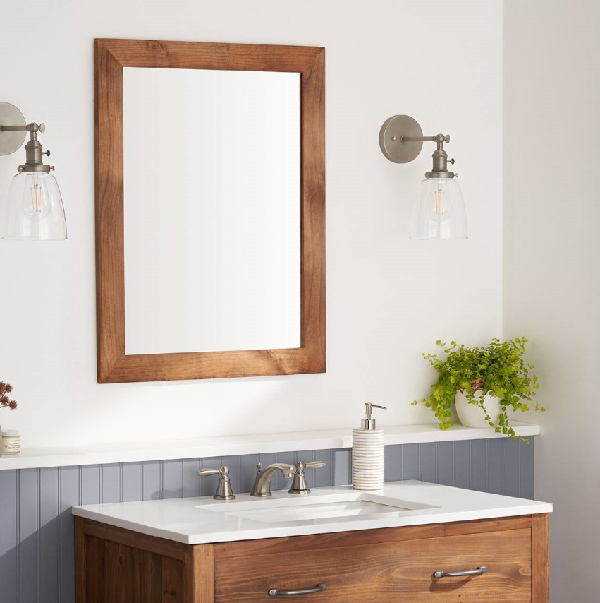 Traditional Bathroom featuring a wooden mirror frame, modern light fixtures, and a clean white countertop.