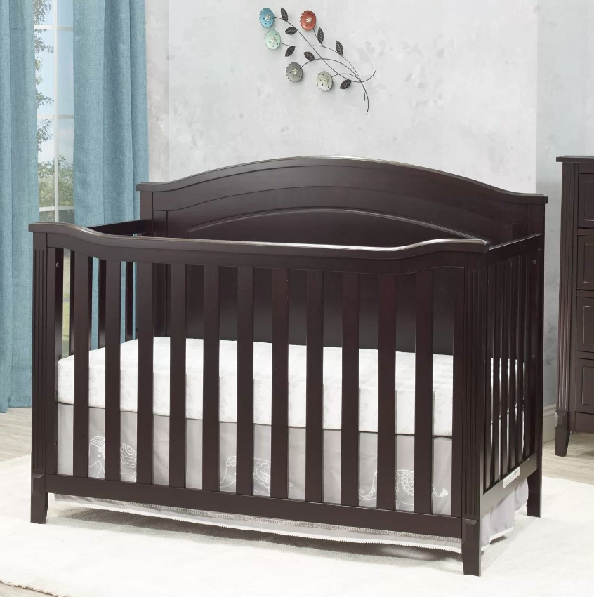 Traditional Nursery brown wooden crib with a mattress in a bright room setting.