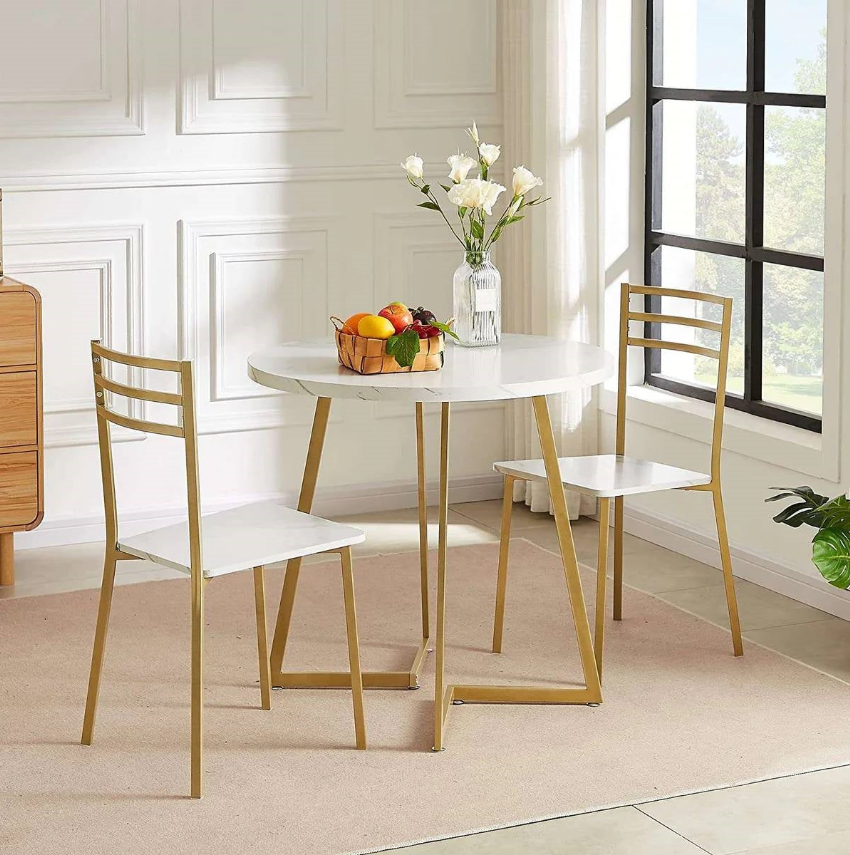 Minimalist Kitchen with a round white table, two gold chairs, and a vase of flowers in a sunlit room.