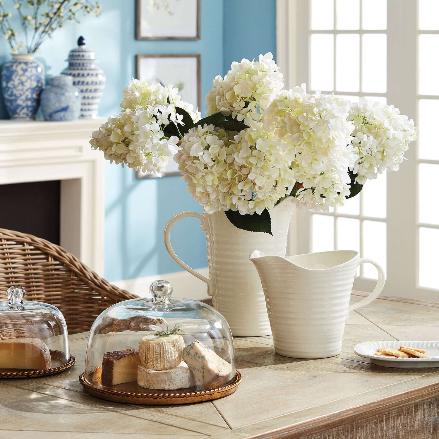 Centerpieces featuring white hydrangeas in a decorative vase on a table with cheese and snacks.
