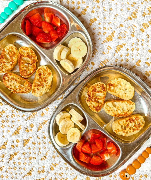 Kids' Dinnerware with delicious food including strawberries and bananas on stainless steel plates.