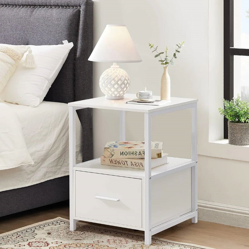 Modern Bedroom nightstand with a lamp, decorative vase, and books beside a gray bed against a bright window.
