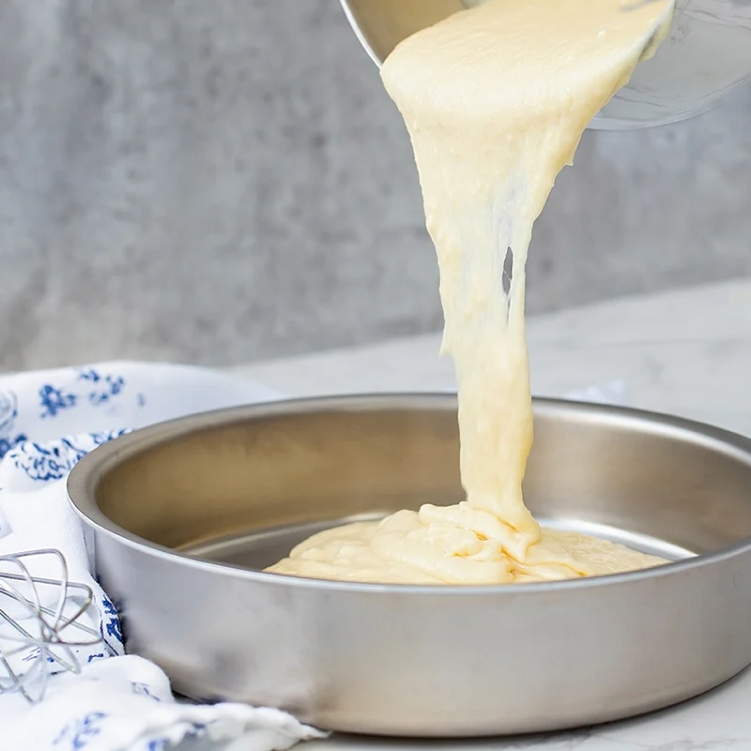 Pouring cake batter into a round metal cake pan in a kitchen setting featuring cake pans.