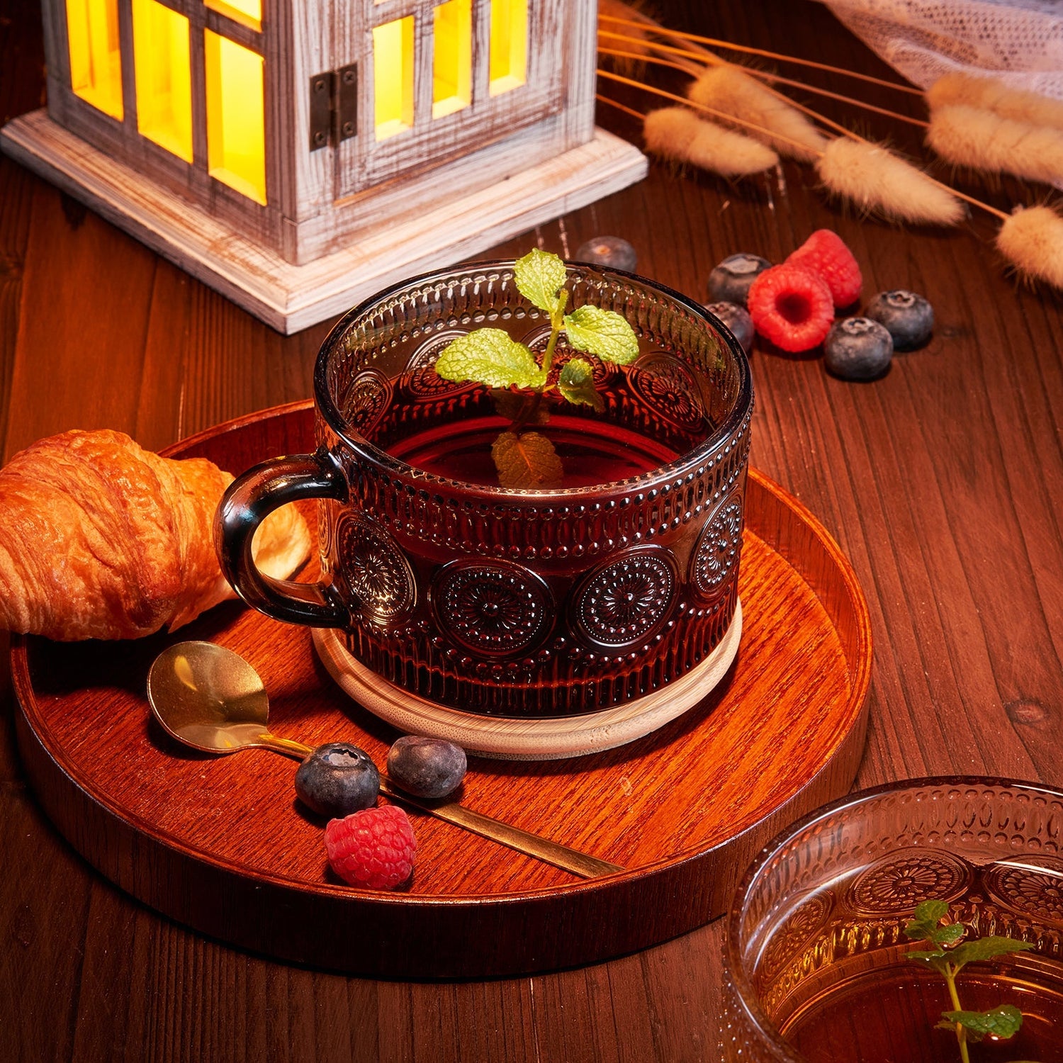 A beautifully styled drinkware setup featuring a dark glass mug with tea, croissant, and fresh berries.