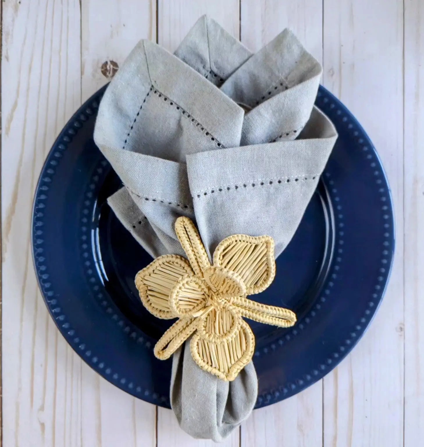 Elegant napkin rings featuring a unique yellow woven flower design on a folded grey napkin.
