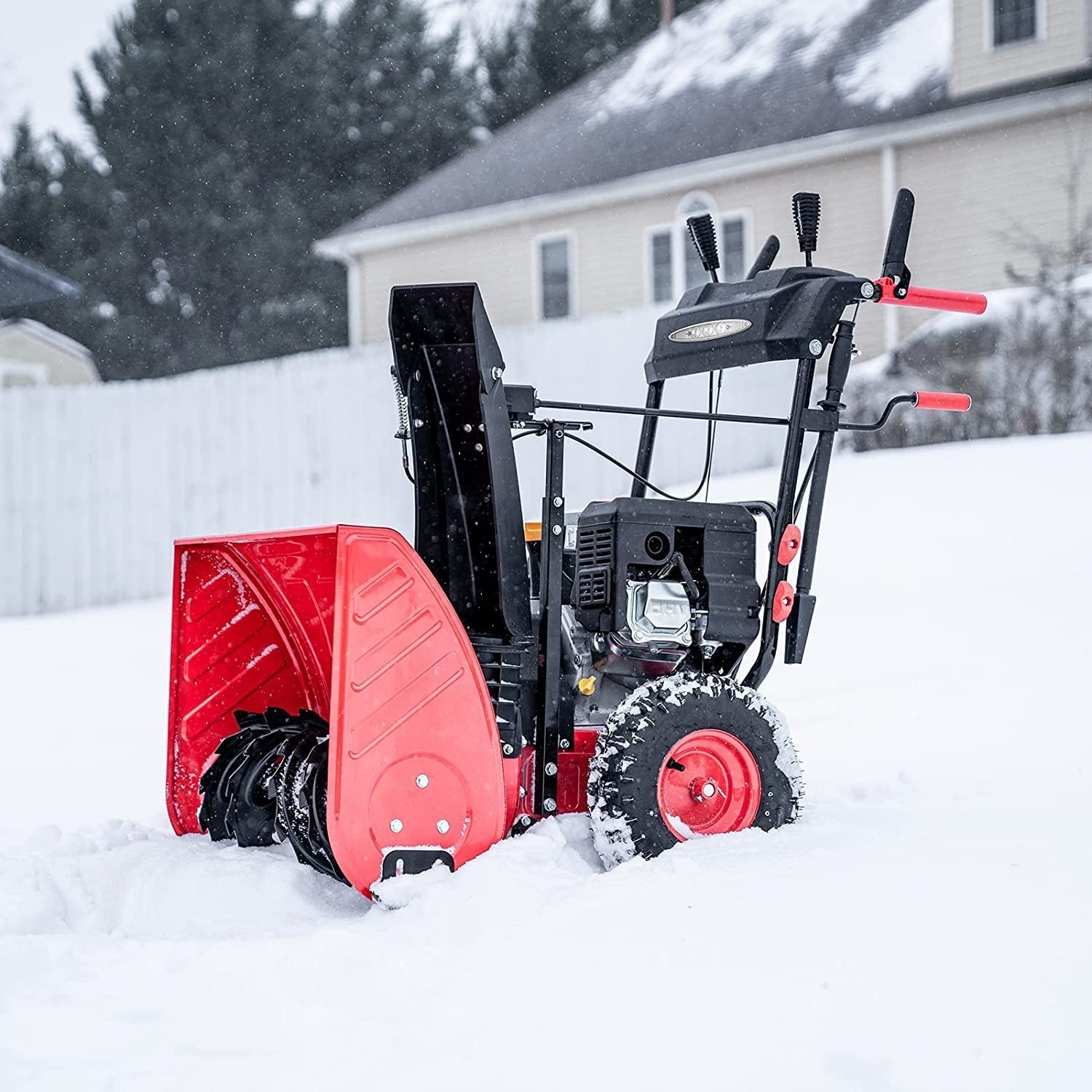 Red snow blower clearing snow in a residential backyard during winter.