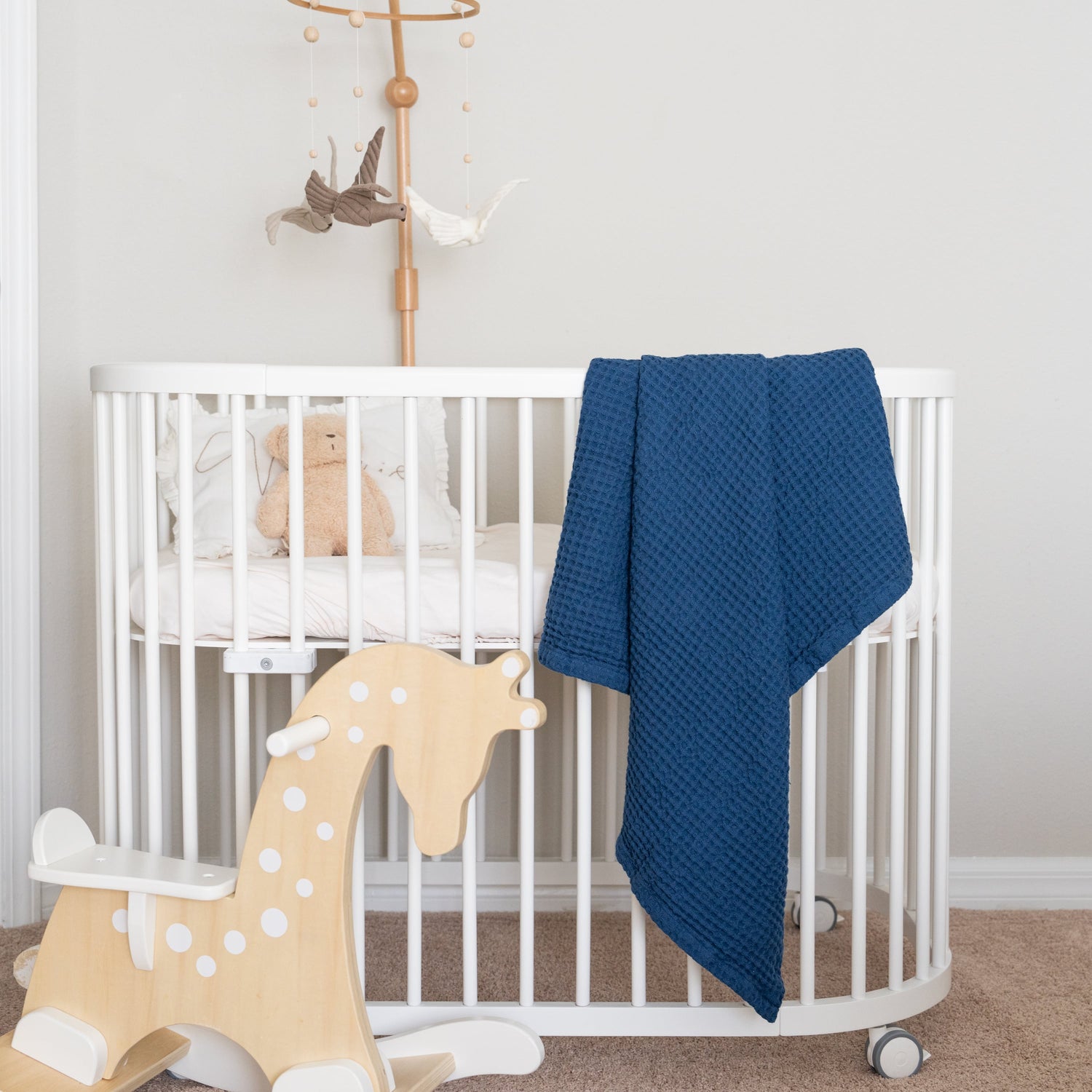 A cozy crib featuring a navy blue baby blanket and a wooden rocking horse, perfect for a nursery setting with baby blankets.
