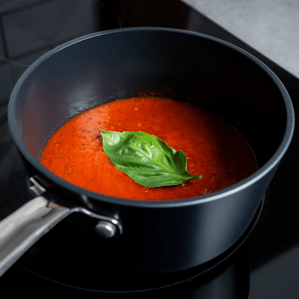 Saucepans cooking rich tomato sauce with fresh basil on top.