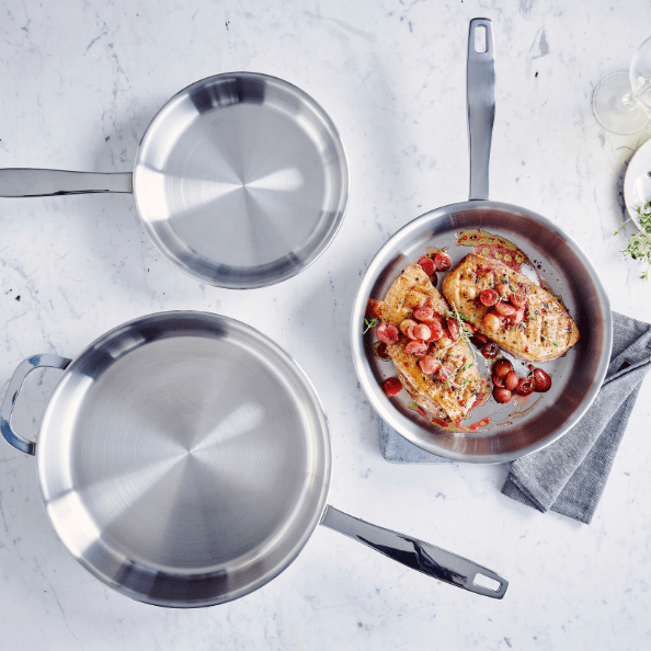 Cookware Sets featuring stainless steel frying pans and a dish of grilled chicken with tomatoes.