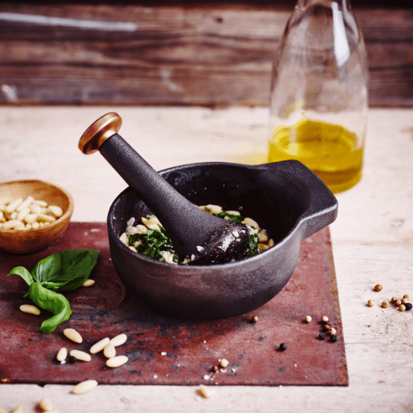 Mortars & Pestles with ingredients like basil, pine nuts, and olive oil on a rustic wooden surface.