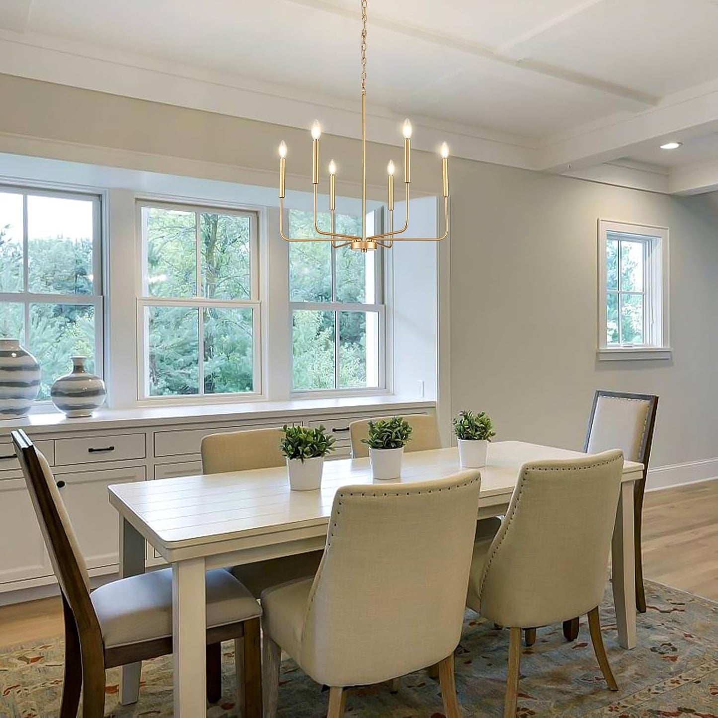 Gold 6 Light Candle Chandelier For Dining Room Modern illuminating a stylish dining room with white furniture and natural light.