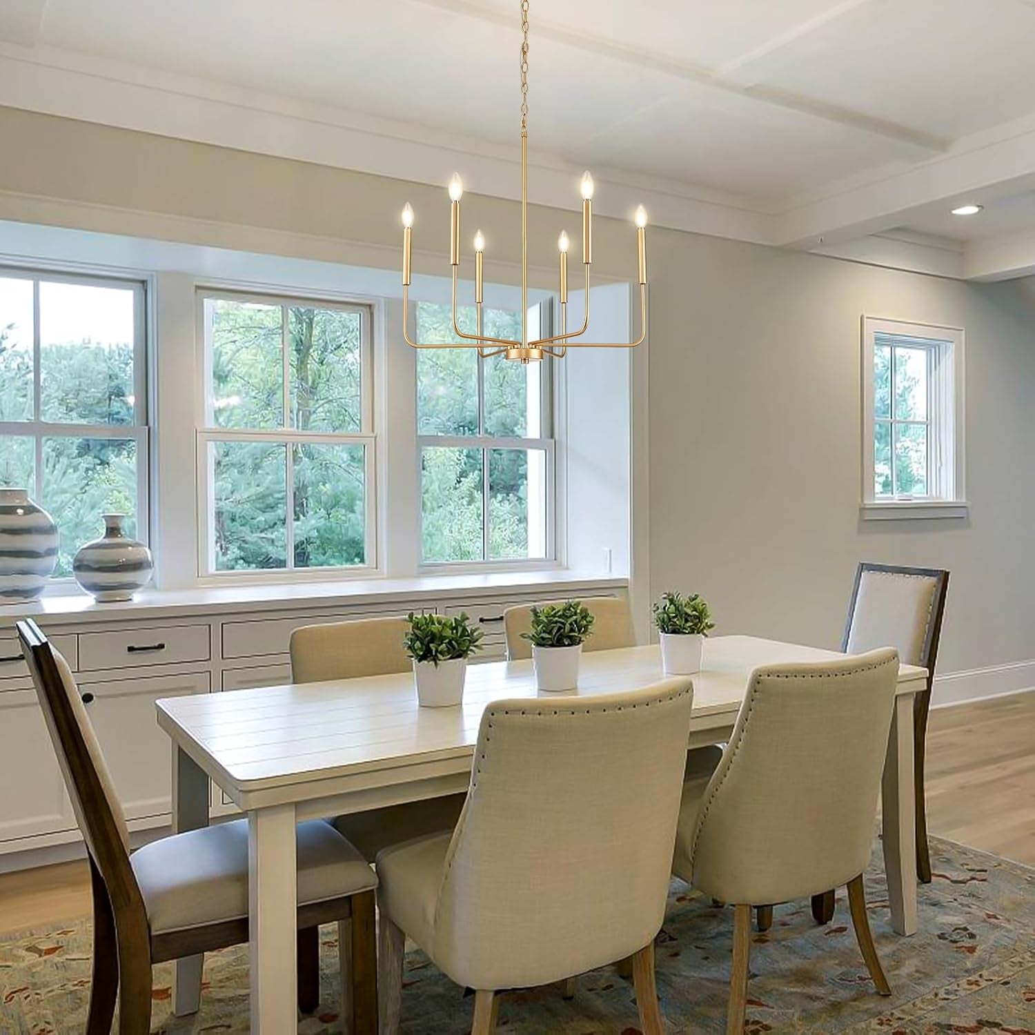 Gold 6 Light Candle Chandelier For Dining Room Modern illuminating a stylish dining room with white furniture and natural light.