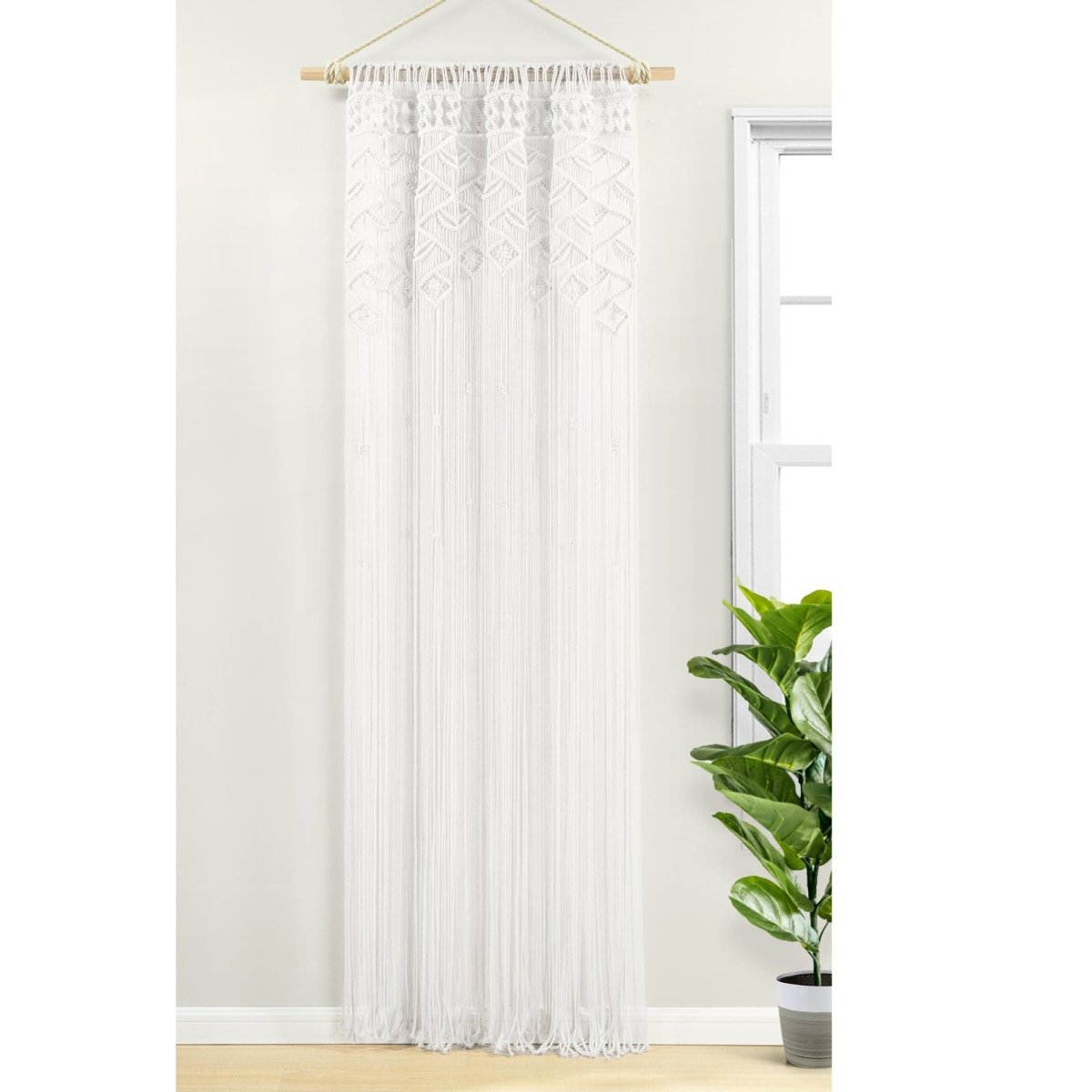 Boho Macrame Leaf Cotton Window Curtain hanging beside a potted plant, showcasing intricate fringe design and natural light filtering.