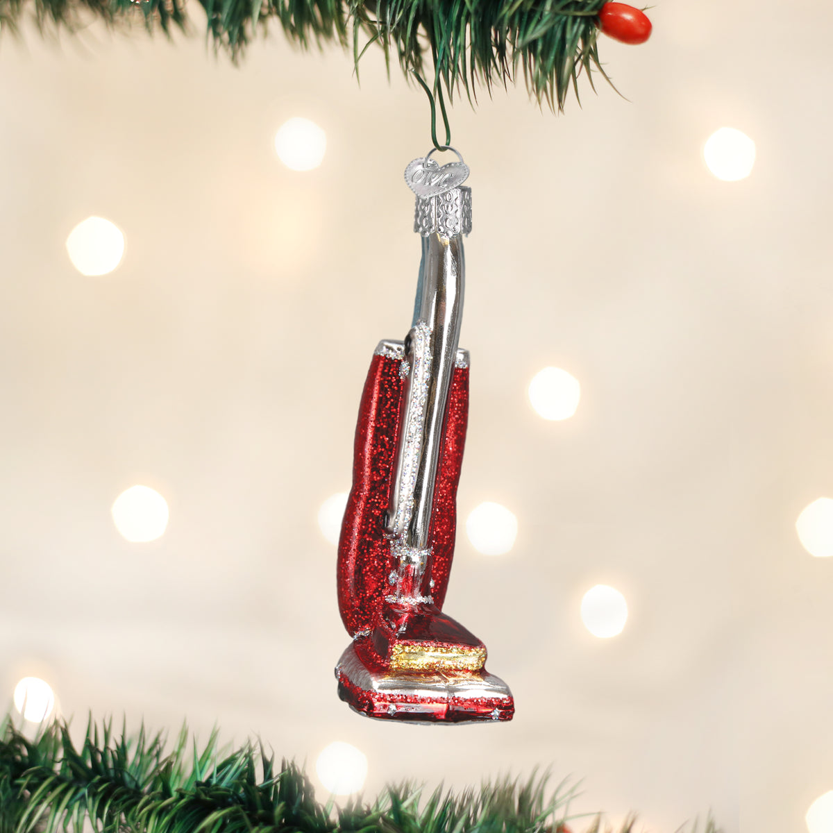 Decorative vacuum cleaner ornament hanging on a Christmas tree with lights in the background.