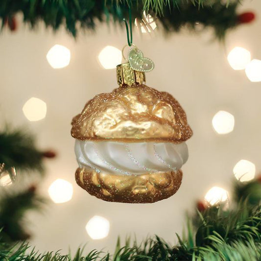 Decorative Christmas ornament shaped like a cream puff with gold and white details, hanging on a tree with lights in the background.
