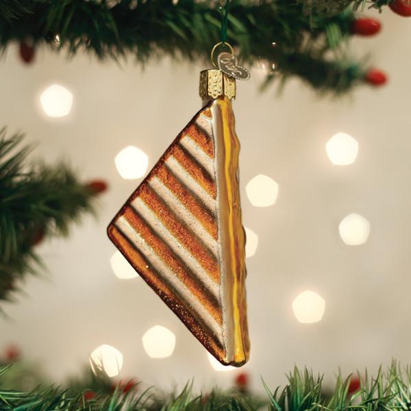 Decorative Christmas ornament shaped like a grilled cheese sandwich on a Christmas tree with lights in the background.
