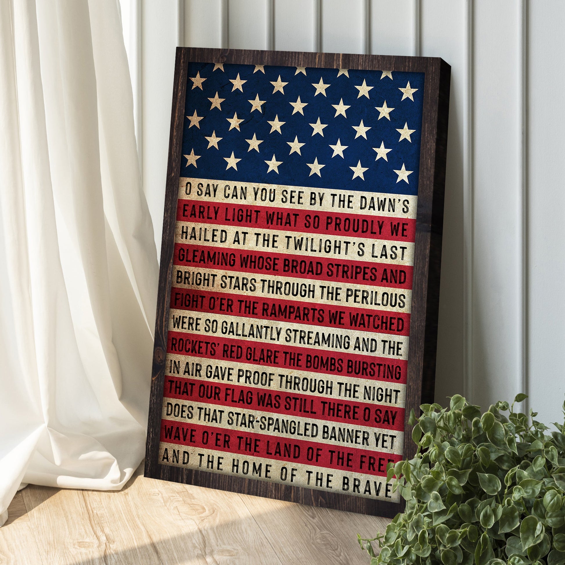 Wooden plaque with American flag design and text on a wooden floor with a plant and curtain in the background.